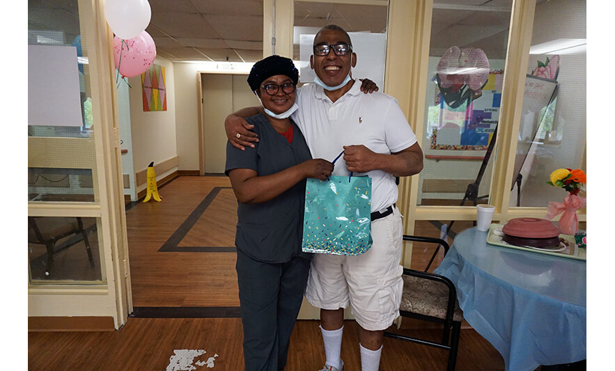 Extended Care Adopt-a-Resident Day 5-11-2022 Female employee giving gift bag to man in glasses for web